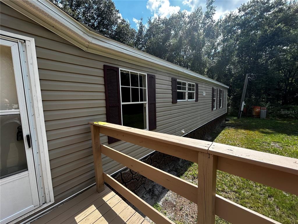 A wooden deck railing overlooks the exterior side of a tan vinyl-sided mobile home — 40838 SUTORUS ROAD, ZEPHYRHILLS, FL