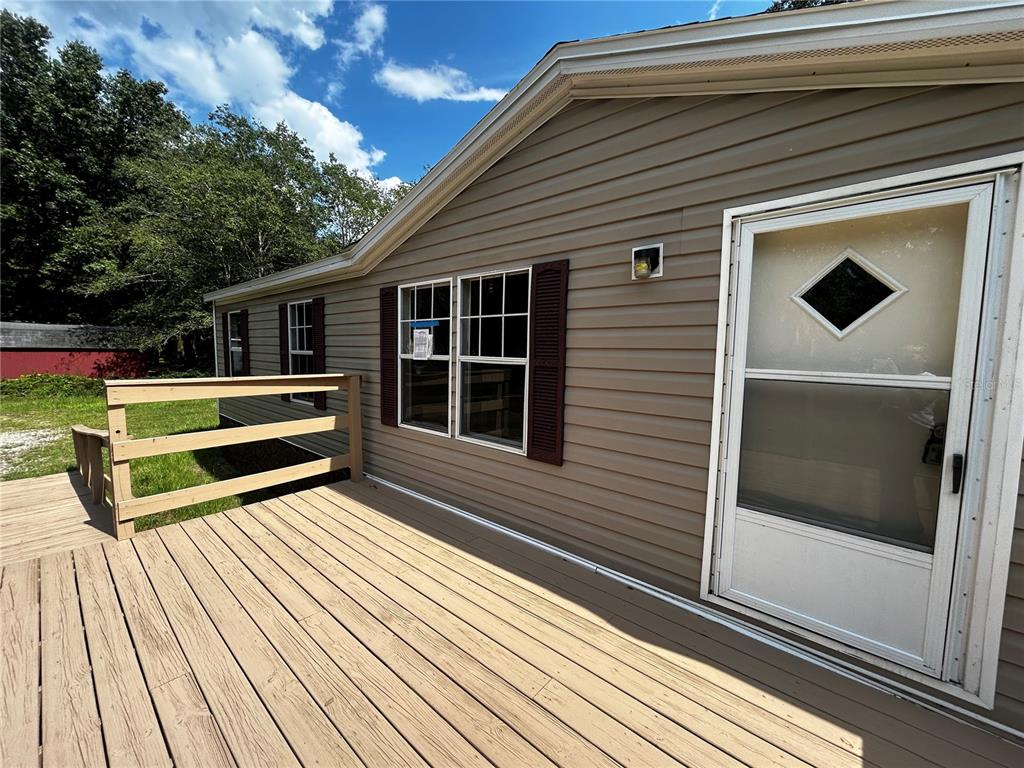 A wooden deck leads to the entrance of a tan vinyl-sided home with shutters — 40838 SUTORUS ROAD, ZEPHYRHILLS, FL