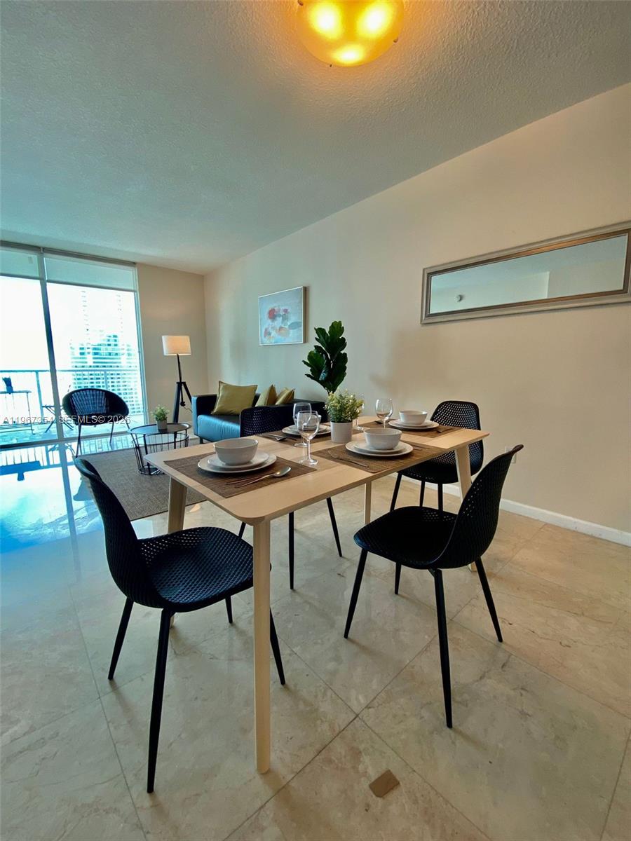 A dining area with a light wood table, four black chairs, and a balcony view — 1200 Brickell Bay Dr # 4217, Miami FL 33131, MIAMI, FL