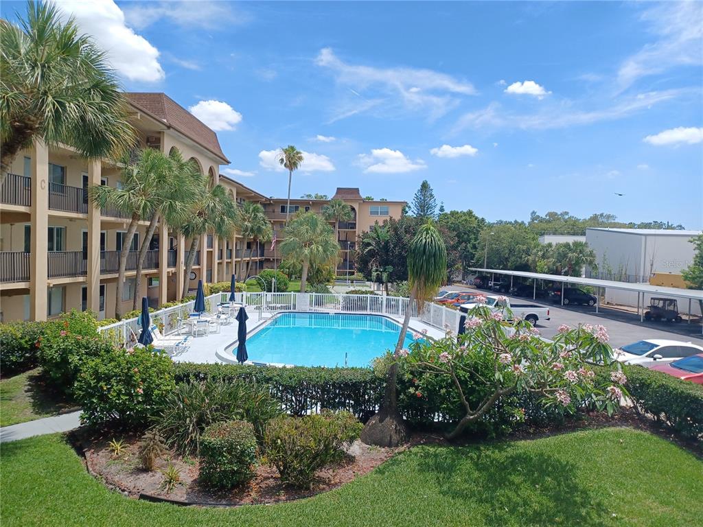 An outdoor swimming pool is surrounded by a white fence, palm trees, and apartment buildings — 2525 W BAY DRIVE UNIT A12, BELLEAIR BLUFFS, FL