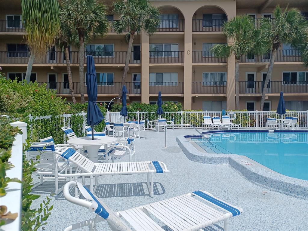 A swimming pool area with lounge chairs, tables, and umbrellas in front of a multi-story building — 2525 W BAY DRIVE UNIT A12, BELLEAIR BLUFFS, FL