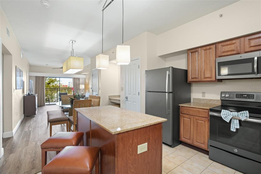 A kitchen with wood cabinets and granite countertops features an island with two leather stools — 12538 FLORIDAYS RESORT DRIVE UNIT 411, ORLANDO, FL