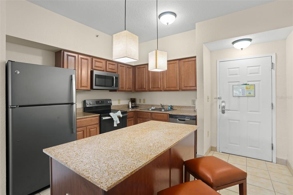 A kitchen features wooden cabinets, granite countertops, a kitchen island, and stainless steel appliances — 12538 FLORIDAYS RESORT DRIVE UNIT 411, ORLANDO, FL