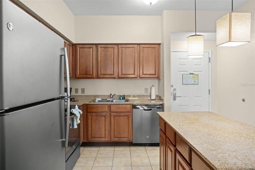 A kitchen features wood cabinets, stainless steel appliances, granite countertops, and a tile floor — 12538 FLORIDAYS RESORT DRIVE UNIT 411, ORLANDO, FL
