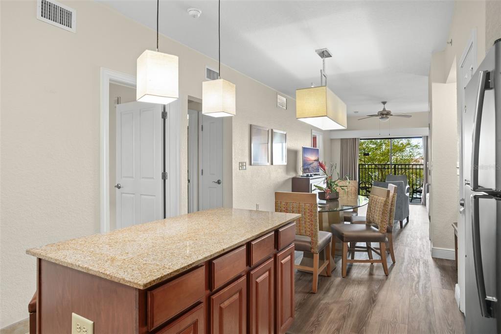A kitchen island with granite countertops overlooks a dining area and a balcony with trees — 12538 FLORIDAYS RESORT DRIVE UNIT 411, ORLANDO, FL
