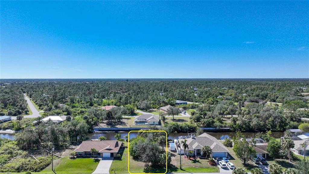 An aerial view shows a vacant, tree-covered residential lot situated between two houses along a canal — 3455 MONTGOMERY DRIVE, PORT CHARLOTTE, FL