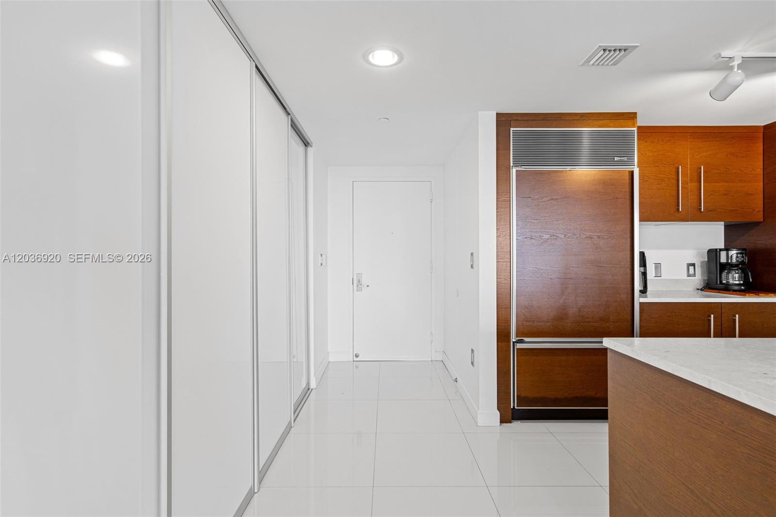 A modern kitchen features white tile floors, wood cabinetry, and a built-in refrigerator — 495 Brickell Ave # 905, Miami FL 33131, MIAMI, FL