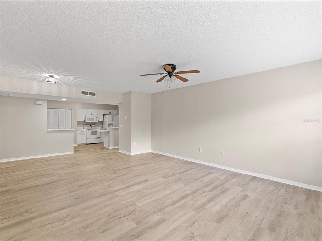 A spacious living room with light wood-look flooring, a ceiling fan, and an adjacent kitchen — 3358 MERMOOR DRIVE UNIT 102, PALM HARBOR, FL