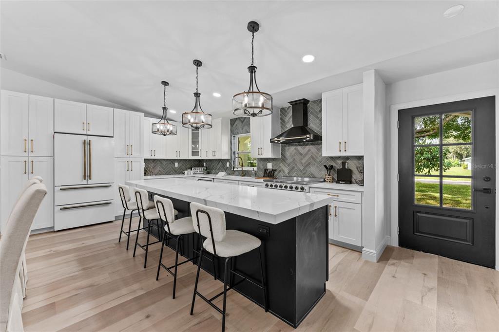 A modern kitchen features white cabinetry, a black island with bar seating, and herringbone backsplash — 10204 TRANQUIL LANE, ODESSA, FL