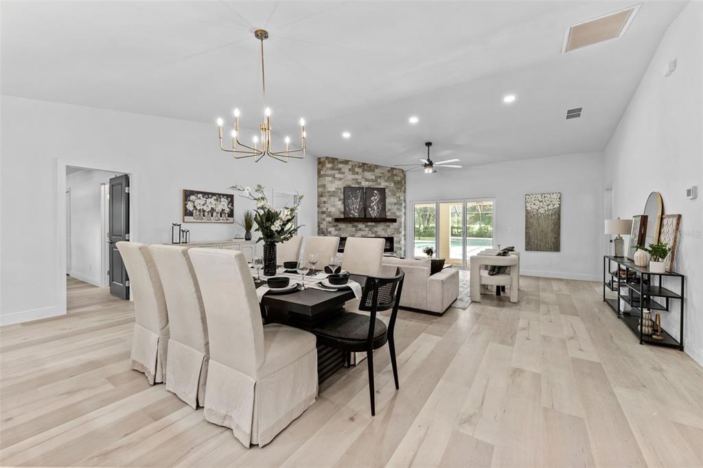 An open-concept living and dining area features light wood floors, a stone fireplace, and chandelier — 10204 TRANQUIL LANE, ODESSA, FL