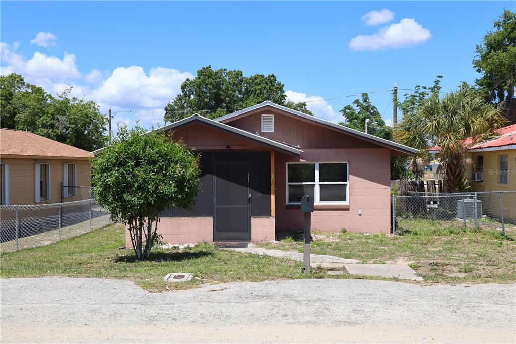 A single-story house with pink stucco walls, a screened front porch, and a gravel driveway — 517 HARRIS STREET, SEBRING, FL