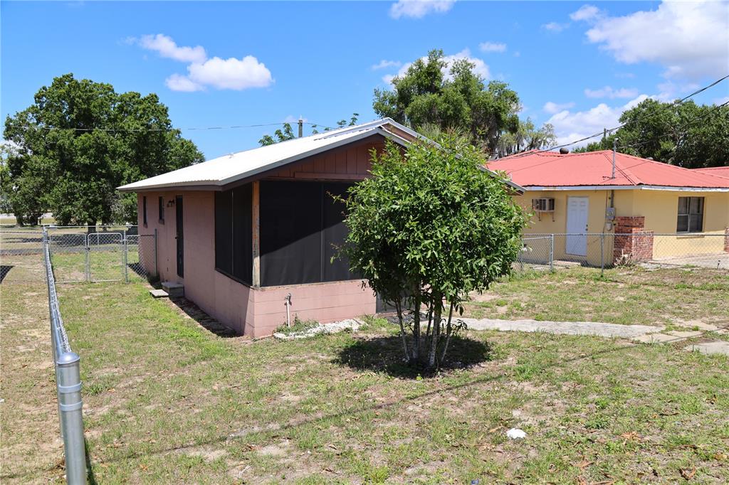 A small, pink, single-story house with a screened-in porch stands in a grassy yard — 517 HARRIS STREET, SEBRING, FL