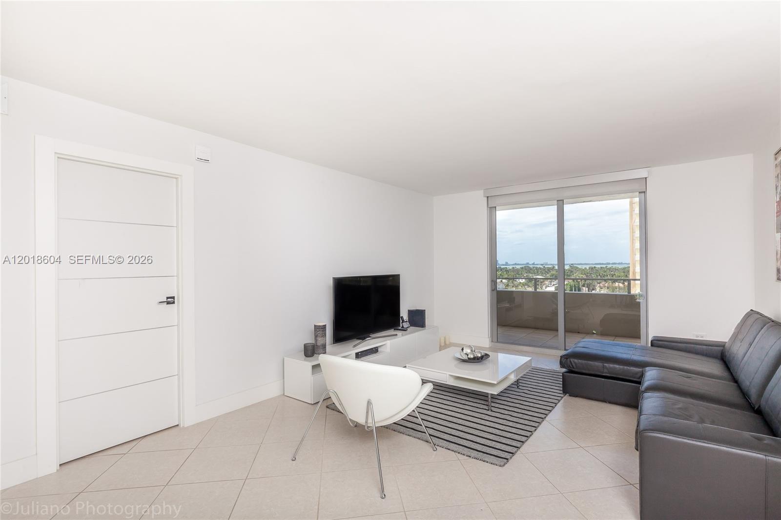 A living room features white walls, tile flooring, a dark leather sofa, and a balcony view — 5555 Collins Ave # 9U, Miami Beach FL 33140, MIAMI BEACH, FL