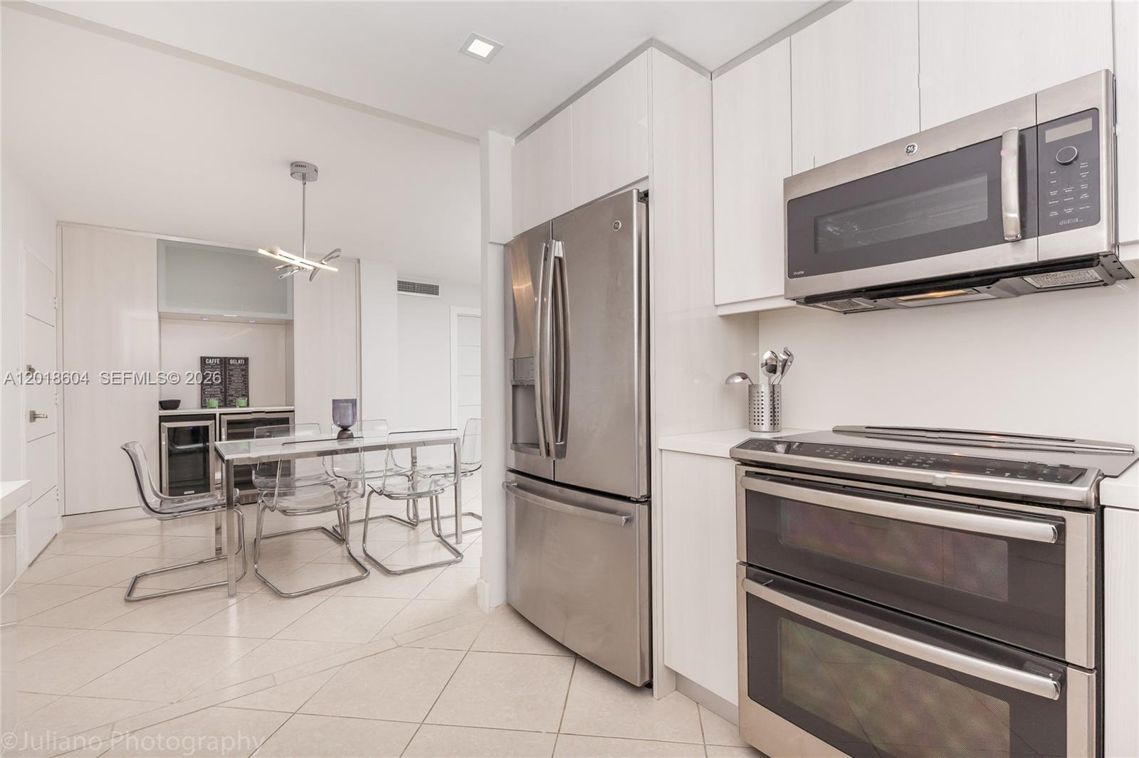 A modern kitchen features stainless steel appliances, white cabinetry, and an adjacent dining area — 5555 Collins Ave # 9U, Miami Beach FL 33140, MIAMI BEACH, FL