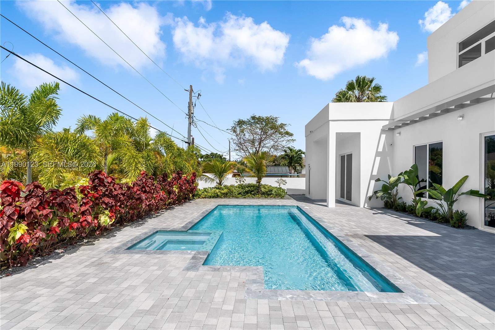 A modern white house features a rectangular swimming pool with an integrated spa on a patio — 9895 NW 26th St, Doral FL 33172, DORAL, FL