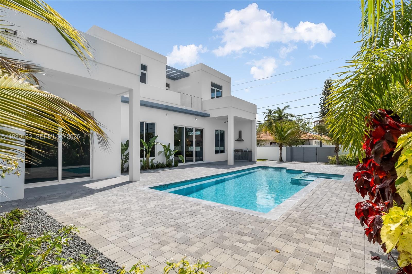 A modern white two-story house features a backyard swimming pool and paved patio area — 9895 NW 26th St, Doral FL 33172, DORAL, FL