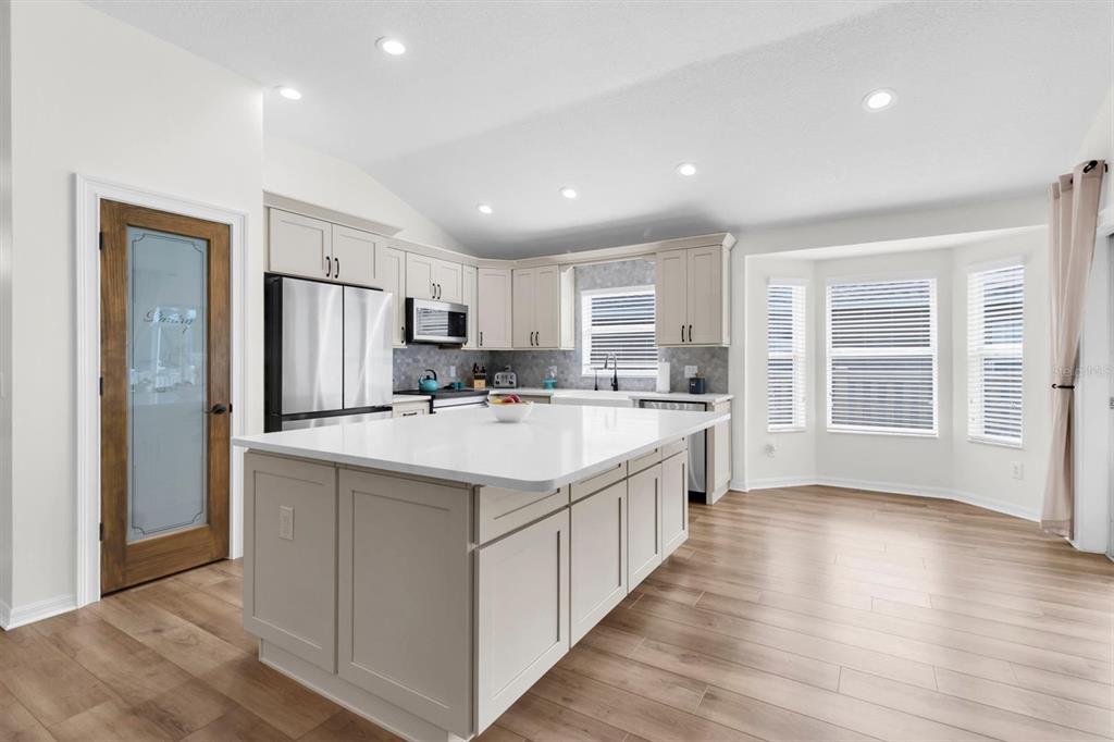 A modern kitchen features light-colored cabinetry, a large white island, and wood-look flooring — 7832 BLUE SPRING DRIVE, LAND O LAKES, FL