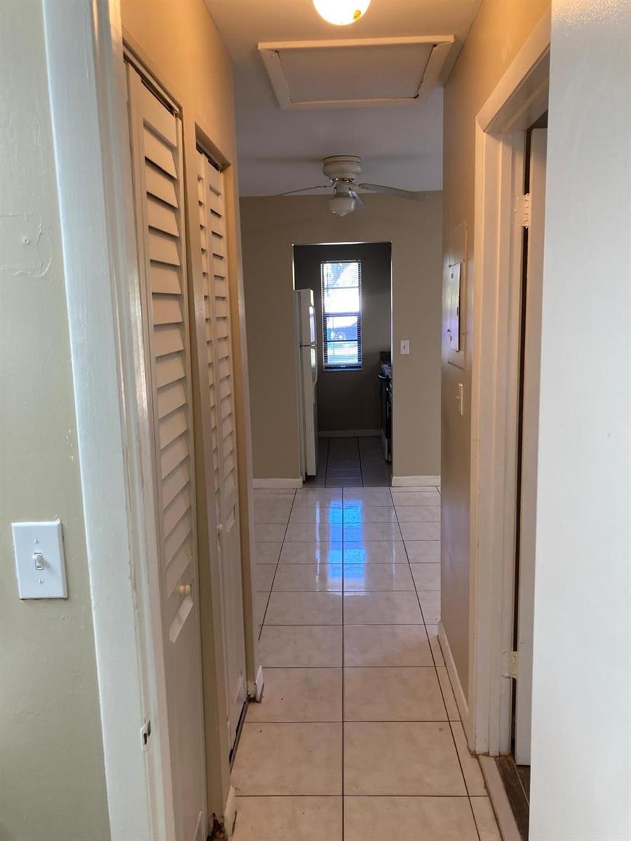 A hallway with white tile flooring leads toward a kitchen with a window — 6148 SW 35th Street # 3, Miramar FL 33023, MIRAMAR, FL