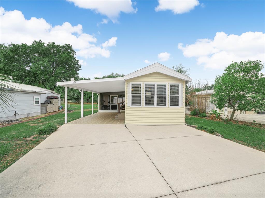 A yellow manufactured home features a concrete driveway, a covered carport, and a screened porch — 6 SILVERSIDES STREET, LAKE WALES, FL