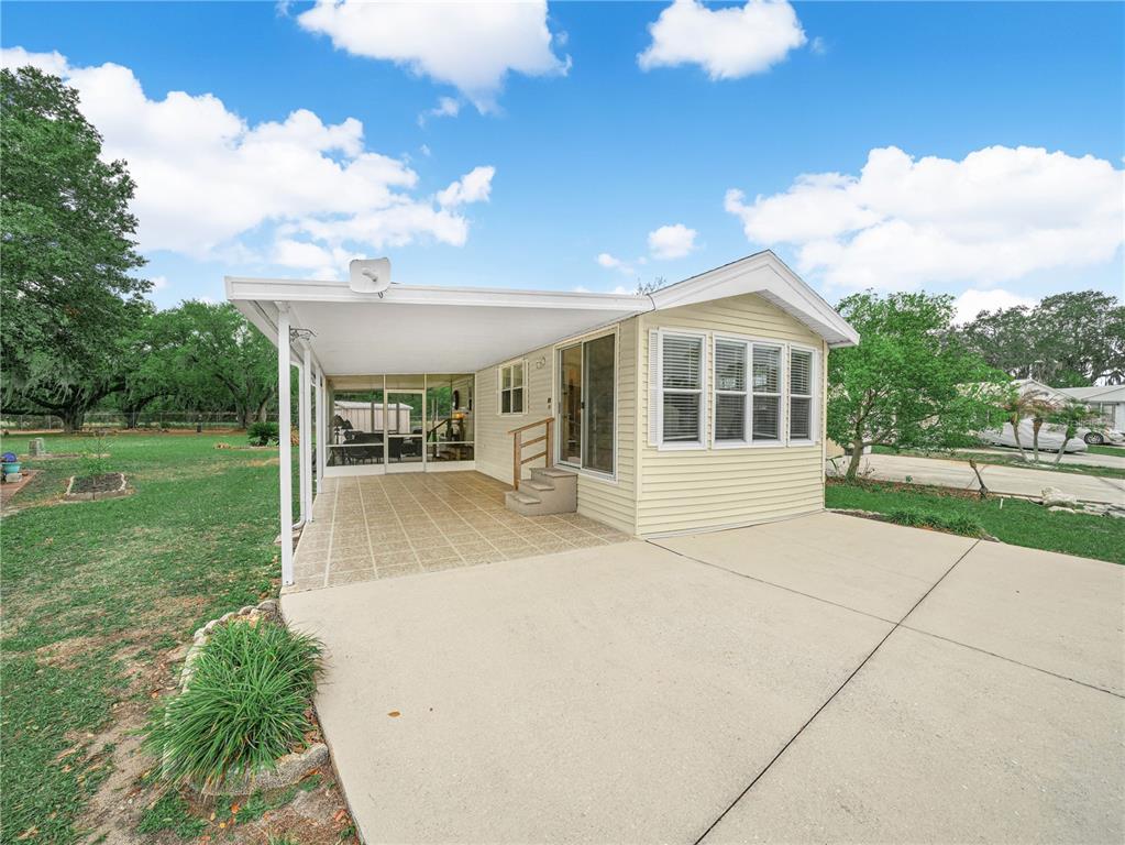 A light yellow mobile home features a covered patio and an attached screened-in porch — 6 SILVERSIDES STREET, LAKE WALES, FL