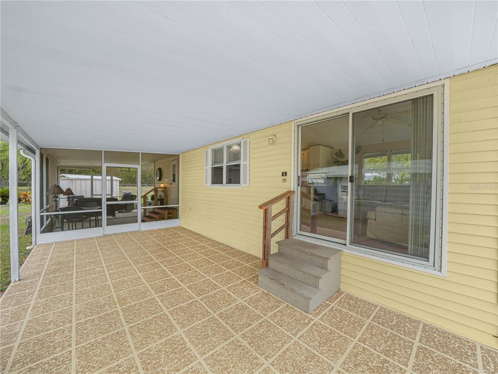 A covered patio with a tiled floor, yellow siding, and a sliding glass door — 6 SILVERSIDES STREET, LAKE WALES, FL