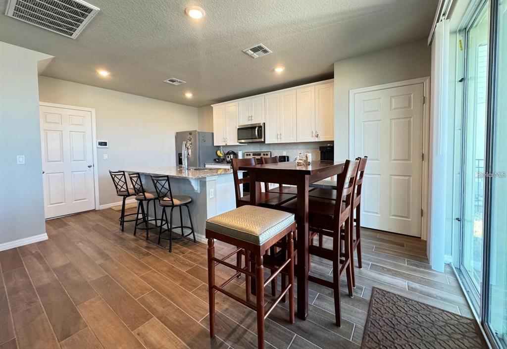 A kitchen features white cabinets, a granite-topped island with bar stools, and wood-look tile flooring — 520 WHISTLING DUCK TRAIL, ST CLOUD, FL
