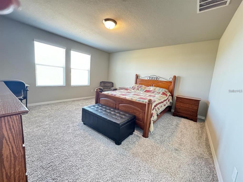 A bedroom features a wooden bed frame, a black storage bench, and wall-to-wall carpeting — 520 WHISTLING DUCK TRAIL, ST CLOUD, FL