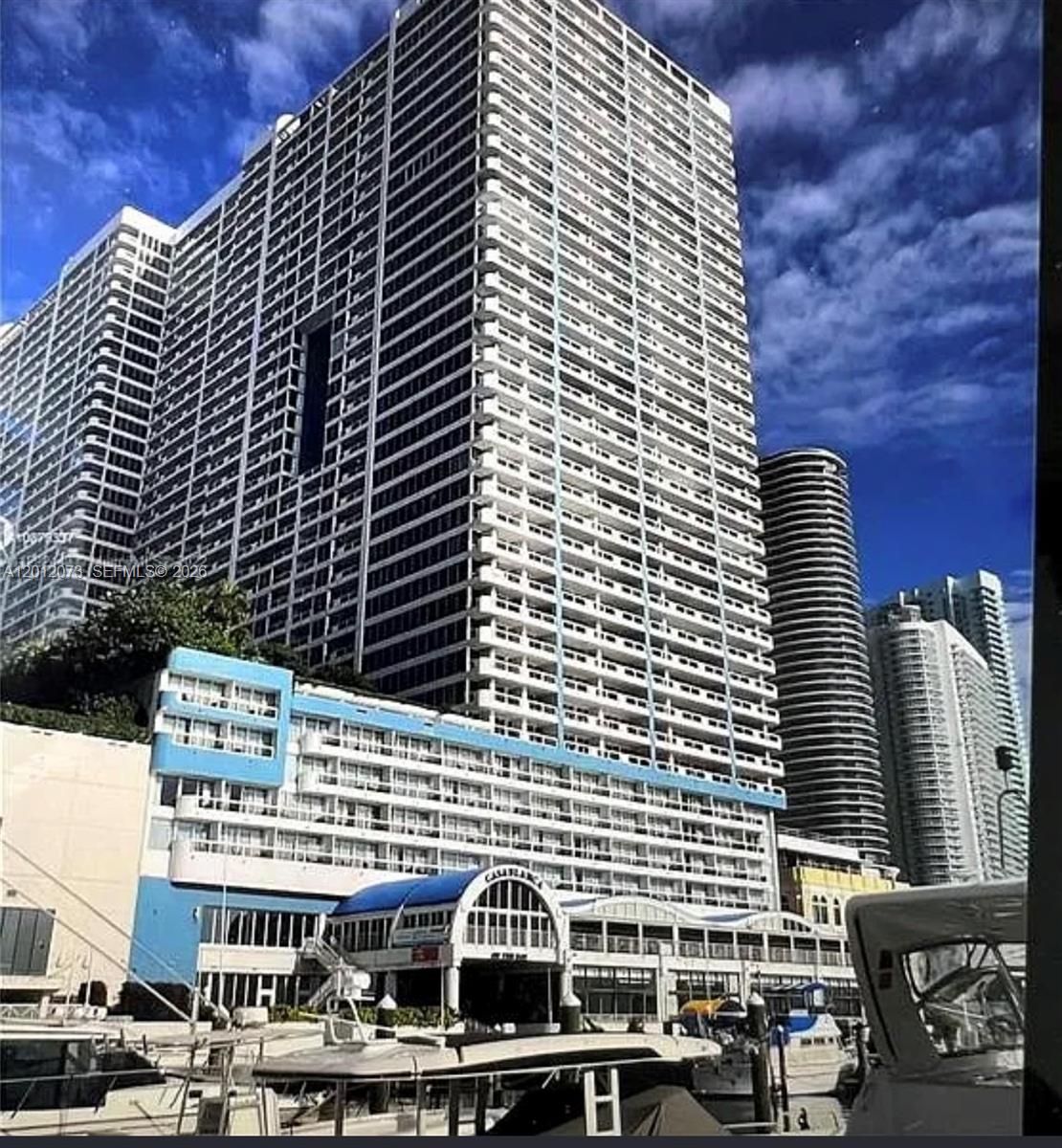 A tall, white high-rise apartment building stands behind a blue-accented waterfront hotel with boat docks — 1717 N Bayshore Dr # A1448, Miami FL 33132, MIAMI, FL