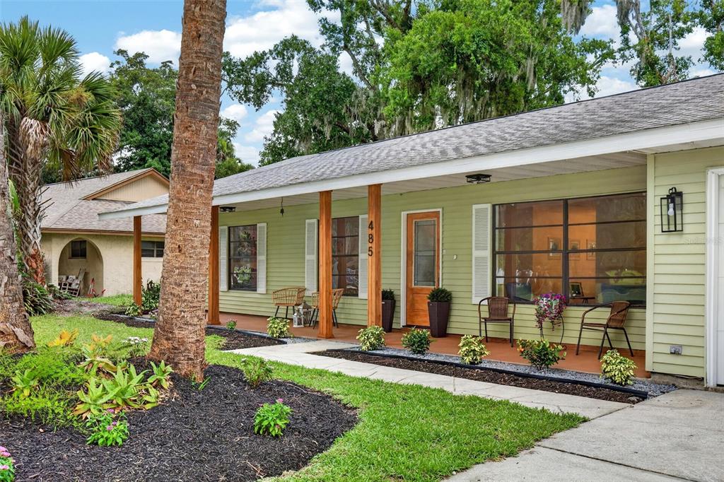 A light green house features a covered front porch with wooden columns and stone landscaping — 485 MERRIMAC DRIVE, PORT ORANGE, FL