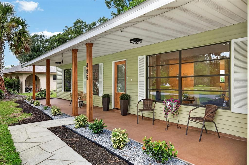 A light green house features a covered front porch with wooden columns and wicker chairs — 485 MERRIMAC DRIVE, PORT ORANGE, FL