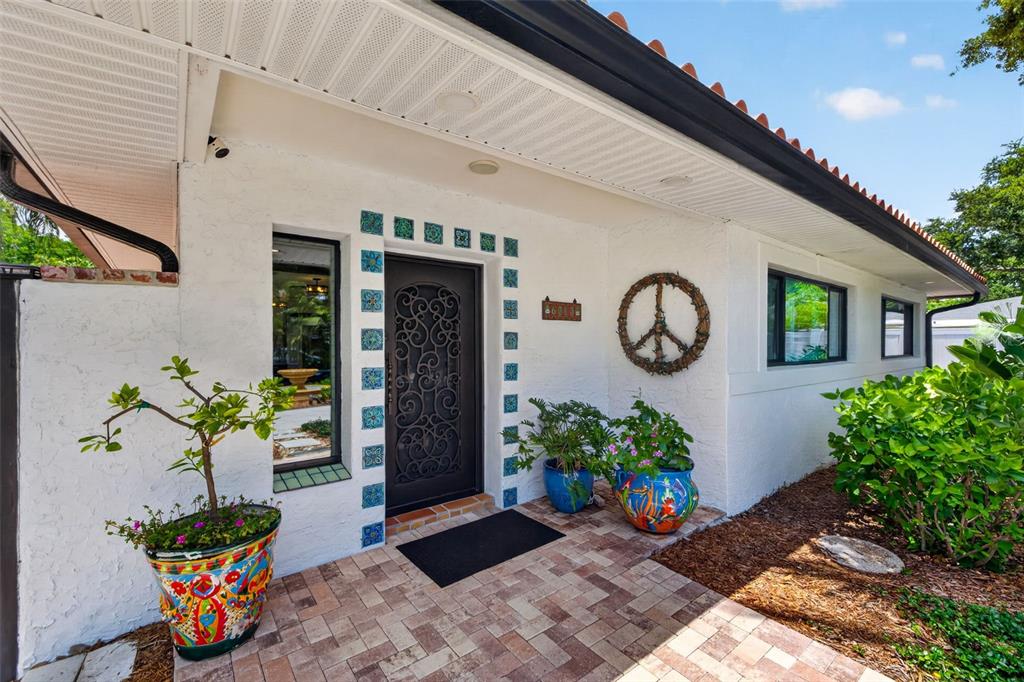 The exterior of a white house features a decorative metal door, tiled trim, and potted plants — 6213 12TH AVENUE S, GULFPORT, FL