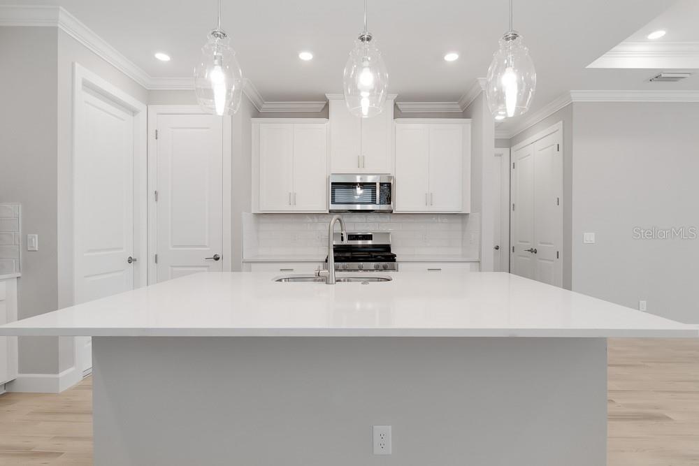 A modern kitchen features a large white island, white cabinetry, and three glass pendant lights — 26930 LARK COURT, PUNTA GORDA, FL