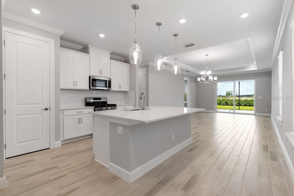 A modern kitchen features white cabinetry, a central island, and light wood-look tile flooring — 26930 LARK COURT, PUNTA GORDA, FL