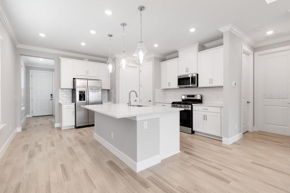 A modern kitchen features white cabinetry, stainless steel appliances, a center island, and light wood flooring — 26930 LARK COURT, PUNTA GORDA, FL