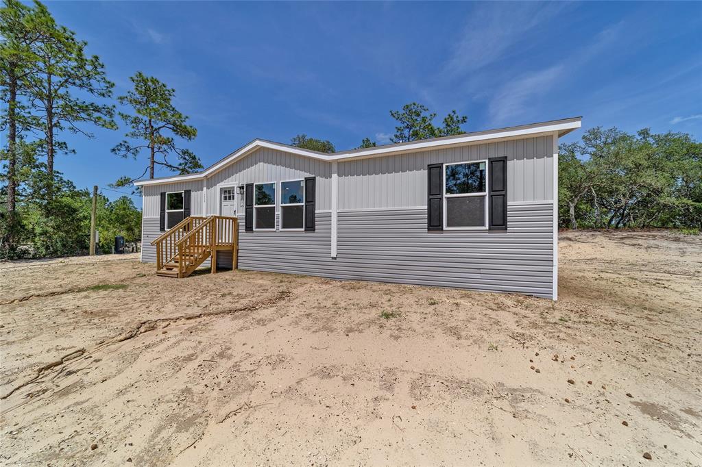 A single-story manufactured home with two-tone gray siding sits on a sandy, undeveloped lot — 14830 SE 21ST PLACE, MORRISTON, FL