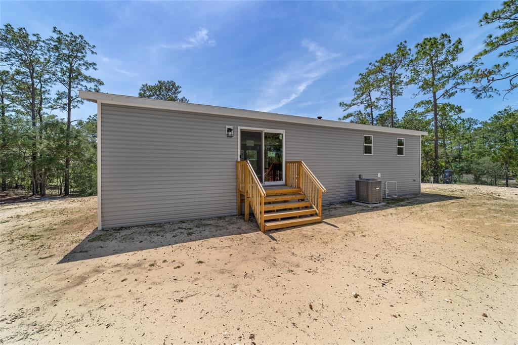 The exterior of a gray-sided house features a wooden staircase leading to a sliding glass door — 14830 SE 21ST PLACE, MORRISTON, FL