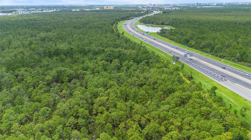 An aerial view shows a large, wooded plot of land adjacent to a multi-lane highway — S APOPKA VINELAND ROAD, ORLANDO, FL