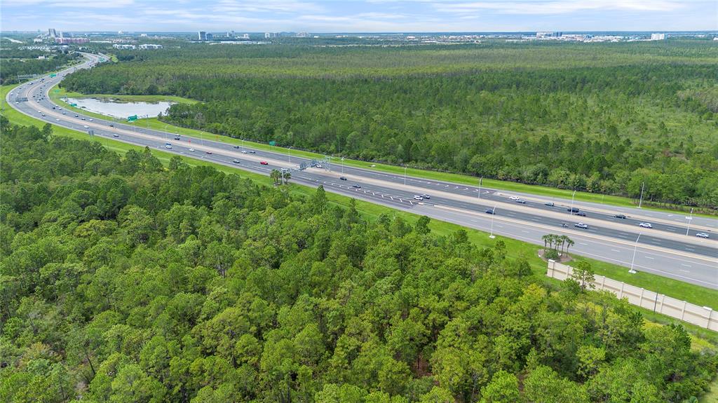 An aerial view shows a multi-lane highway curving through a dense forest with a small pond — S APOPKA VINELAND ROAD, ORLANDO, FL