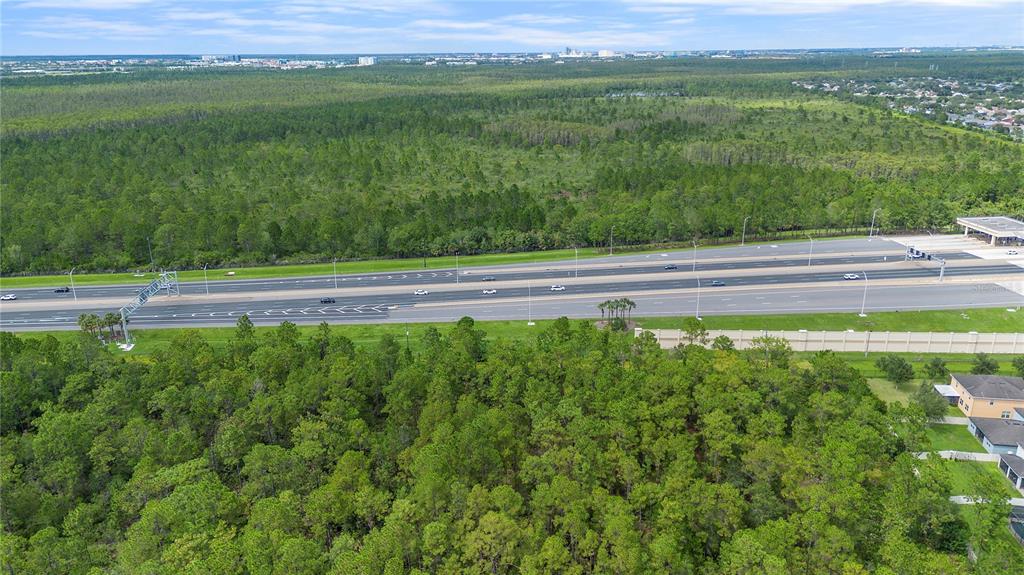 An aerial view shows a multi-lane highway running between dense wooded areas and residential homes — S APOPKA VINELAND ROAD, ORLANDO, FL