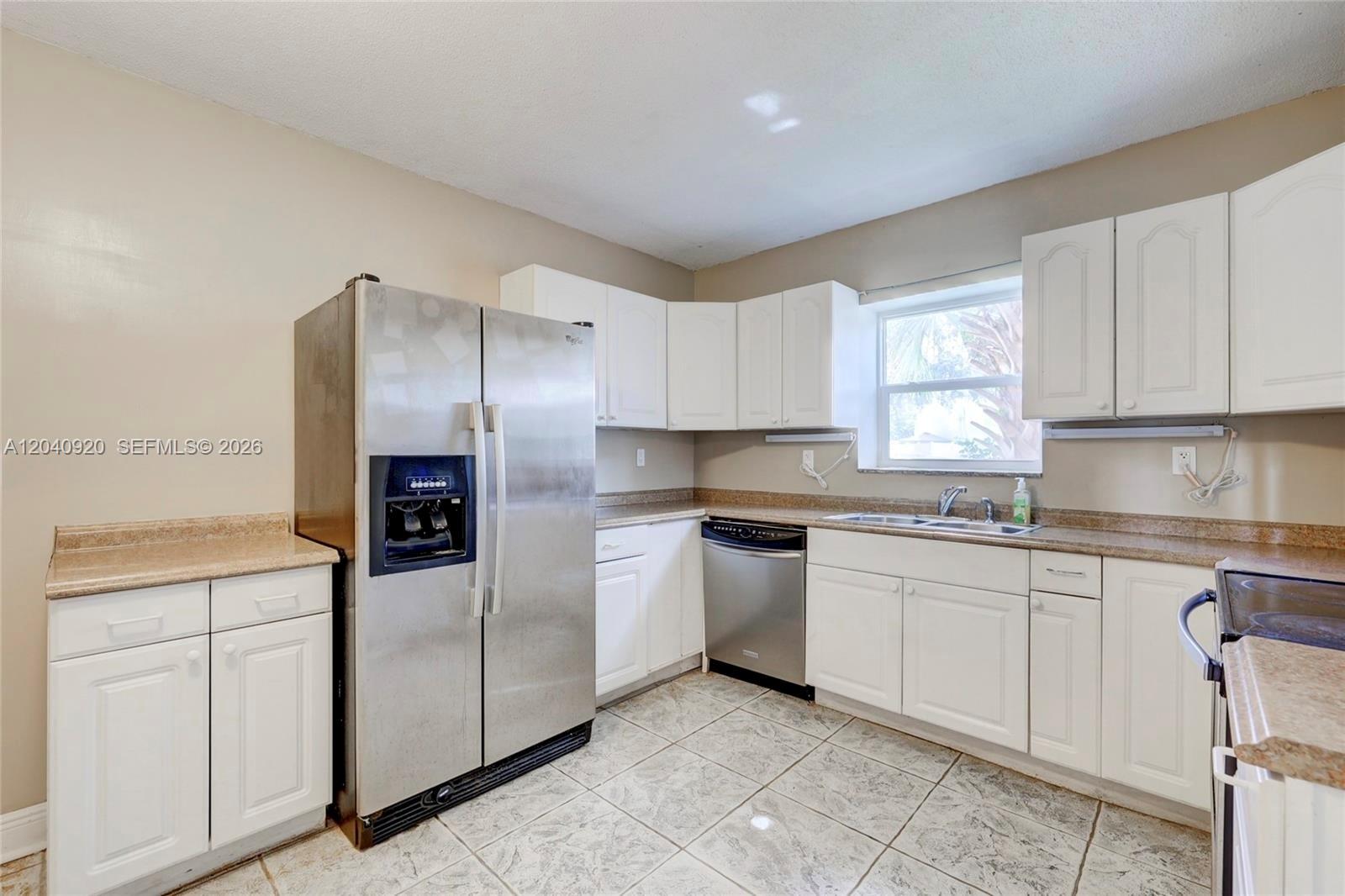A kitchen features white cabinets, stainless steel appliances, tan countertops, and light-colored tile flooring — 350 Sunshine Dr, Coconut Creek FL 33066, COCONUT CREEK, FL