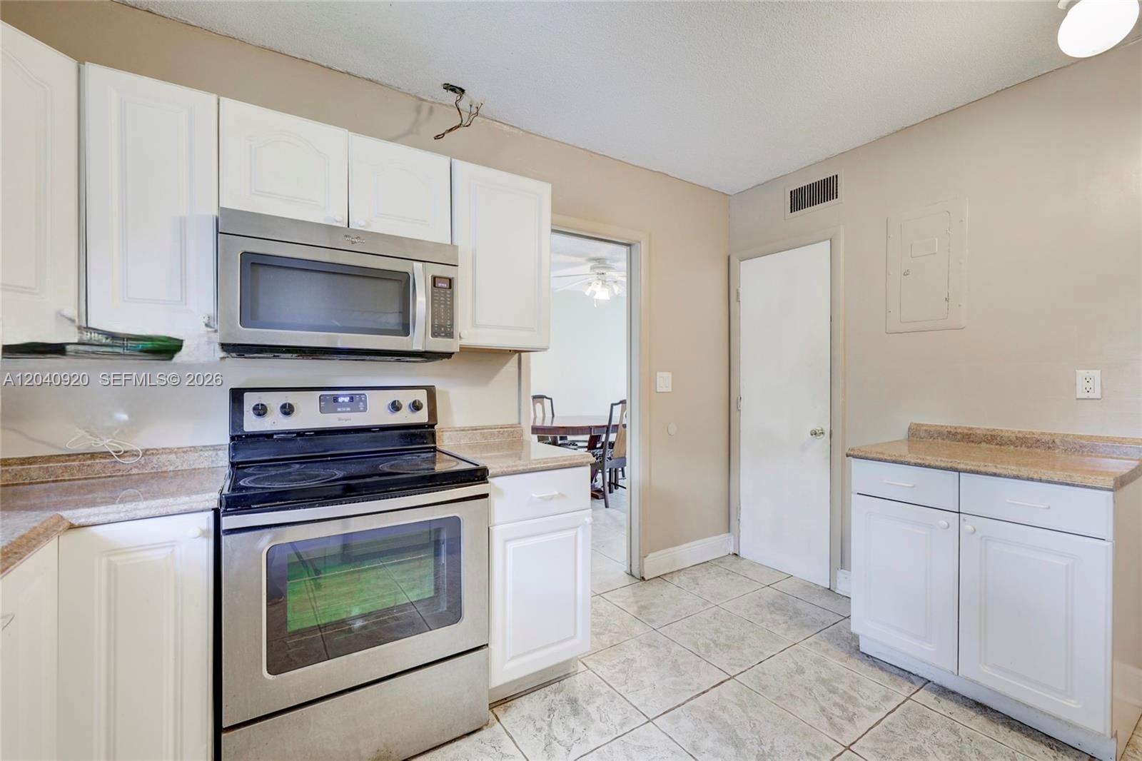 A kitchen features white cabinets, stainless steel appliances, tan countertops, and light-colored tile flooring — 350 Sunshine Dr, Coconut Creek FL 33066, COCONUT CREEK, FL
