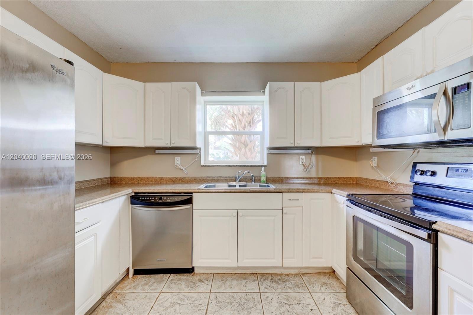 A kitchen features white cabinets, stainless steel appliances, tan countertops, and light-colored tile flooring — 350 Sunshine Dr, Coconut Creek FL 33066, COCONUT CREEK, FL