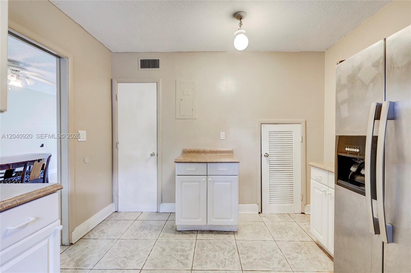A kitchen features white cabinets, a small island, tiled floors, and a stainless steel refrigerator — 350 Sunshine Dr, Coconut Creek FL 33066, COCONUT CREEK, FL