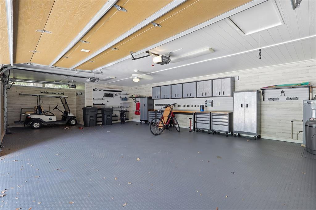 A spacious garage features a gray floor, white paneled walls, storage cabinets, and a golf cart — 29922 BAYWOOD LANE, WESLEY CHAPEL, FL