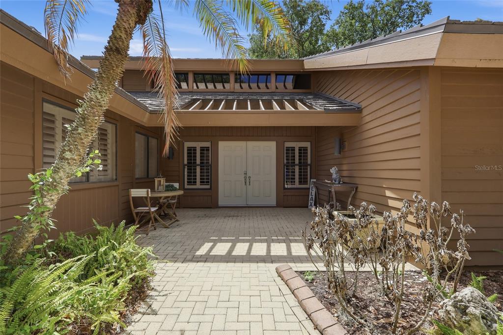 A paved walkway leads to the double front doors of a brown wood-sided house — 29922 BAYWOOD LANE, WESLEY CHAPEL, FL