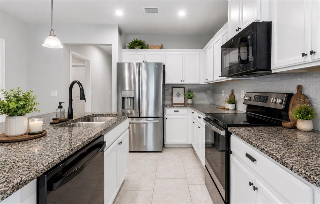 A kitchen features white cabinets, granite countertops, stainless steel appliances, and a black faucet — 18307 TURNING LEAF CIRCLE, LAND O LAKES, FL
