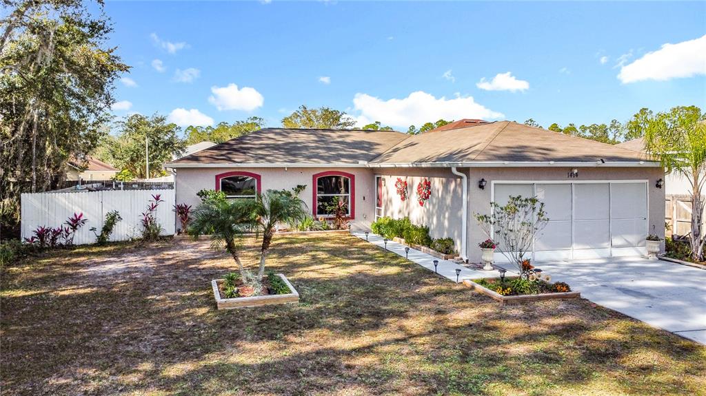 A single-story house with a beige exterior, red window trim, and a two-car garage — 1414 SWAN COURT, POINCIANA, FL
