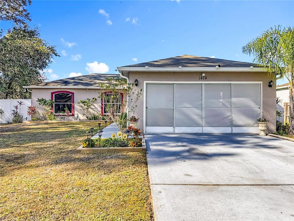 A single-story house with a beige exterior, a three-panel garage screen, and a front garden — 1414 SWAN COURT, POINCIANA, FL