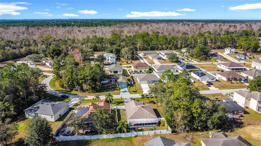 An aerial view shows a suburban neighborhood with houses, driveways, and surrounding wooded areas — 1414 SWAN COURT, POINCIANA, FL