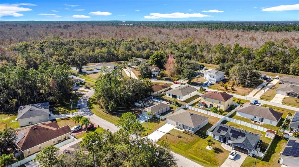 An aerial view shows a suburban neighborhood with single-family homes surrounded by dense forest — 1414 SWAN COURT, POINCIANA, FL